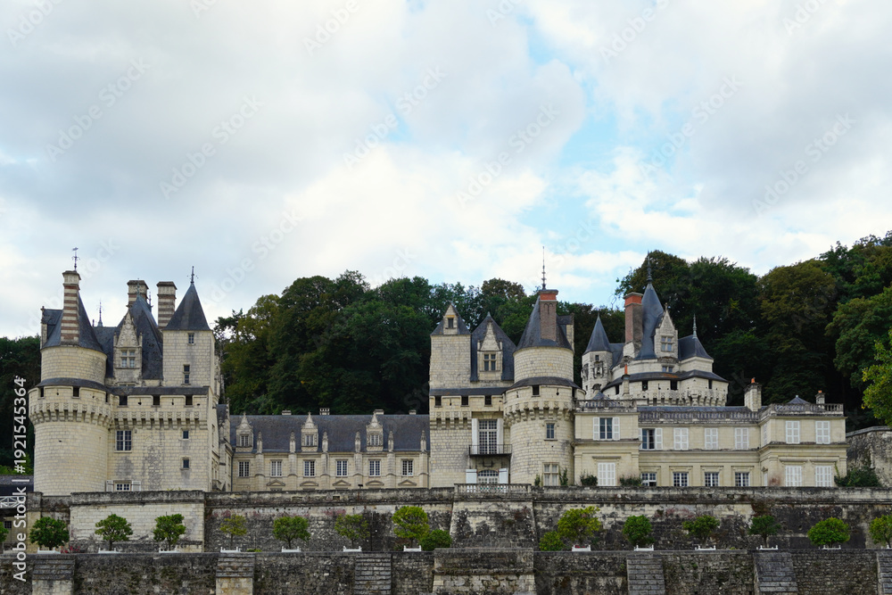 Fototapeta premium View of the Château d'Ussé rising above the river with a stone bridge in the foreground. Elegant French architectural landmark featuring historic towers, fortified walls, and landscape