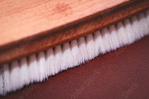 Extreme close-up macro photography focusing on the detailed soft white bristles and wooden handle of a cleaning or grooming brush on a brown textured background.
