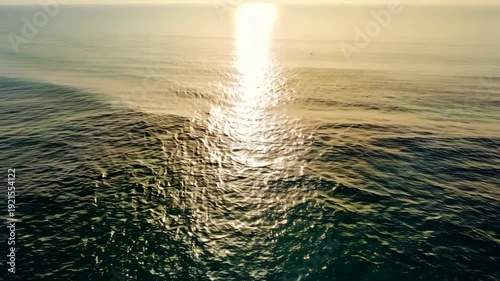 Sunlight reflects off calm ocean waves, creating a shimmering pathway across the water surface during a serene sunset over the horizon