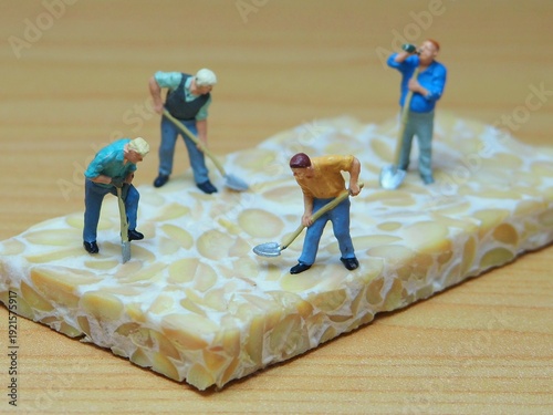 Mini toy of action figure at table with blur background. Miniature photography concept design. Minifigure of farmer crew character with tempe. Agriculture theme at farmland. Tempe is traditional food.