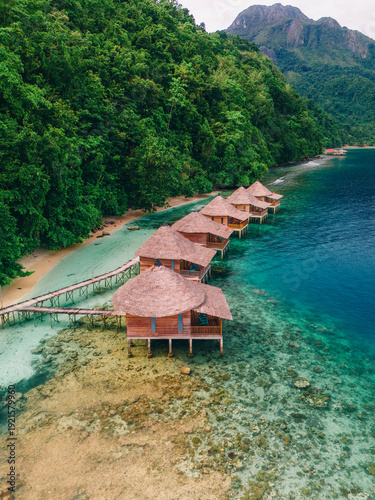 Drone aerial view of Sawai coastal village surrounded by turquoise lagoon and tropical mountains in Seram Island, Maluku, Indonesia.