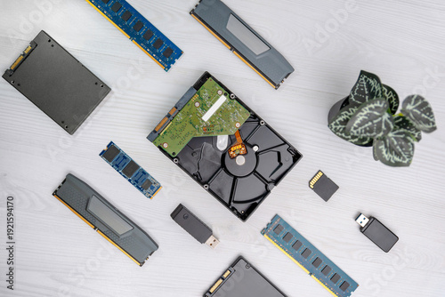Open hard disk drive with visible platter, RAM modules, SSD, USB flash drive and memory card arranged in flat lay on light desk