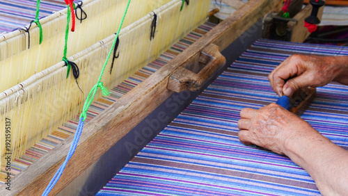 A craftsman tying plastic strings on silk threads to create traditional Thai Mudmee (ikat) patterns before dyeing. Handmade silk weaving process showing Thai culture, craftsmanship, and textile art.