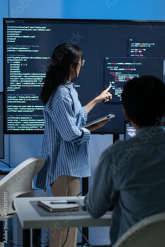 Foto Asian Female Developer presenting code to Colleagues or Team Explaining code and discussing on software development task during code meeting or software training, Cybersecurity in office at night