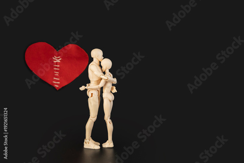 Conceptual image of two plastic mannequins hugging each other and on background a large red heart with stitches, symbolizing reconciliation, healing a broken heart, and saving a relationship