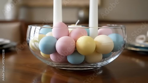 Vibrant pastel Easter eggs nestled in a clear glass bowl with tall white candles, creating a festive springtime table centerpiece, symbolizing renewal, celebration, and the Easter holiday