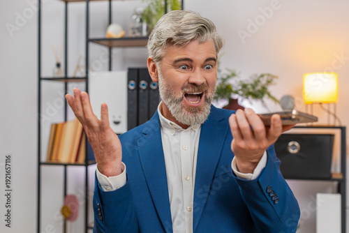 Photos Middle-aged businessman at home office on smartphone speakerphone argues with supplier over shipment delay