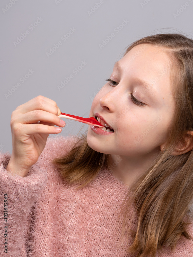 Obraz premium Smiling girl holding gummy candy and looking at camera in studio. Sweet snack, happy child, colorful treat, dessert time, playful 