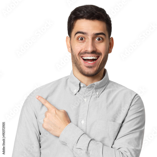 Excited young man in grey shirt with wide eyes and big smile pointing sideways, no glasses