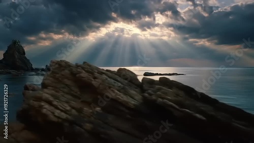 Dramatic seascape with sun rays through clouds over ocean and rocks