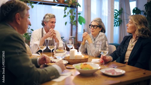 Group of elegant older friends talking and laughing together. Happy senior people having a pleasant dinner party in a cozy candlelit room