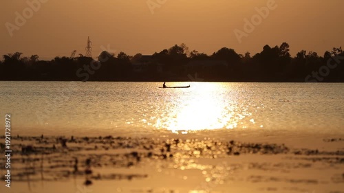 A beautiful summer evening landscape features a vibrant red and orange sunset sky reflecting over the calm water of a nature river and lake horizon at dusk