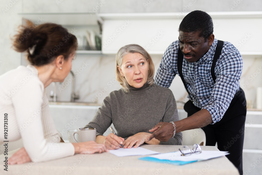 Obraz premium Middle-aged family members partitioning inheritance with mother sitting at kitchen-table with a sheet of paper and pen in hand