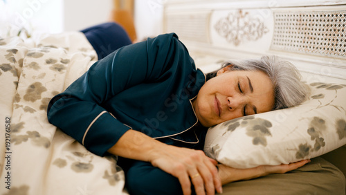 Senior woman resting comfortably in bed, wearing pajamas, enjoying a peaceful night's sleep in a cozy bedroom
