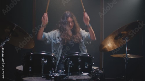 Portrait: female drummer hits drum kit, finishes rehearsal. Music band repetition. Woman with long curly hair, drumming in studio, rock live concert. Modern hobby, art skill. Slow motion