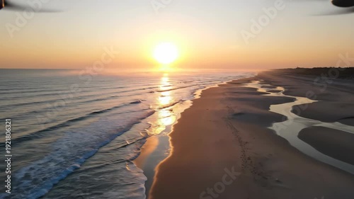 Sunrise over tranquil beach with gentle waves lapping at the shore, reflecting golden light on the sand and water, creating a serene coastal landscape