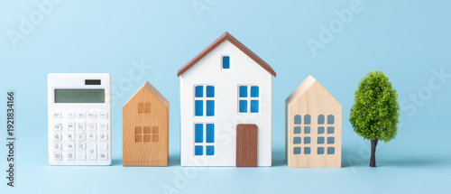 Real estate investment concept with calculator, wooden house models, and tree on blue background, symbolizing property value and financial planning