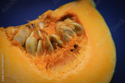 Fresh pumpkin slice close up with seeds, orange squash macro on blue background