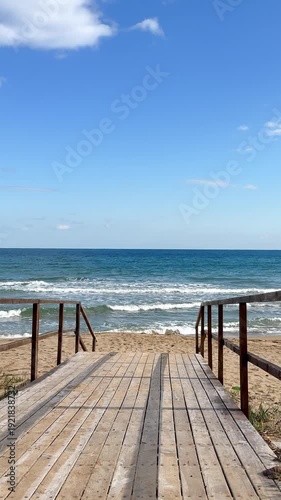 Wooden boardwalk leading to a quiet sandy beach with gentle waves and a blue sea. Sunlight casts creating a serene path to the ocean. Perfect for coastal relaxation and nature-inspired travel concepts