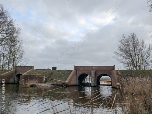 фотографія sluice gate in a Dutch polder landscape under a grey winter sky