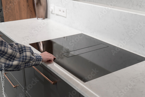 Woman's hand touching black induction cooktop with integrated extractor