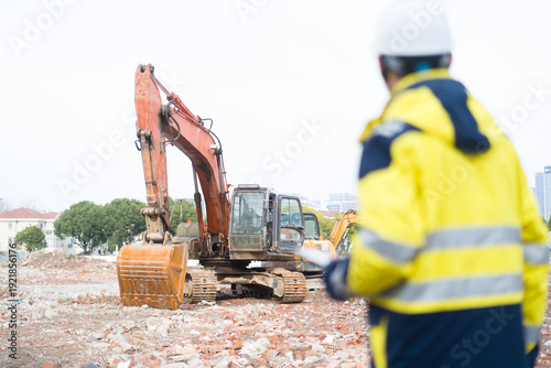 Photos Construction worker in high-visibility uniform supervising orange excavator oper