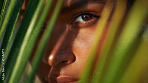 Close up of a womans eye looking through tropical palm leaves for exotic summer vacation and beauty concepts