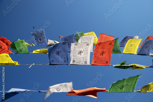 Colorful Tibetan prayer flags flutter in the wind at a Buddhist temple beneath a bright blue sky during midday