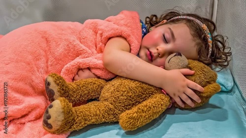 A little girl sleeps hugging a teddy bear