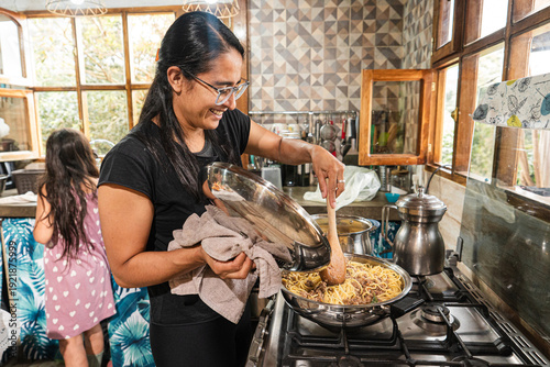 Photos Mother mixing pasta with sauce in cozy kitchen while daughter stands nearby