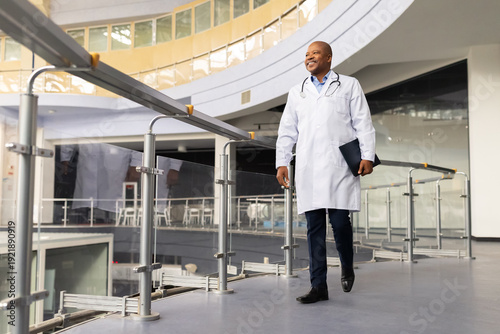 Photography Mature black doctor walking in modern hospital atrium with folder, confident afr