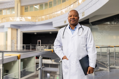 Photos Mature black doctor standing in hospital atrium holding folder, confident medica