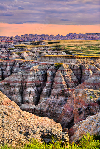 Big Badlands Overlook stands in Badlands National Park, South Dakota, USA. Scenic view features colorful eroded rock formations and sedimentary layers under a cloudy sunset sky