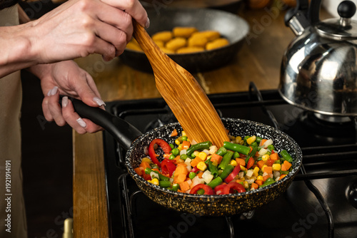 Bild auf Leinwand Person Stirring Vegetables in Frying Pan on Kitchen Stove