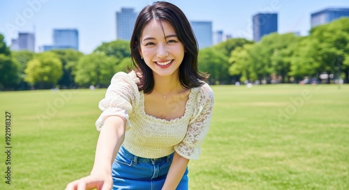 晴天の芝生広場で手を繋ぎこちらを振り向く笑顔の女性