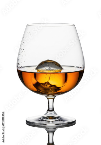 A flawless crystal snifter of aged single malt whiskey with a sphere ice cube on a reflective white background. Concept of premium spirits and luxury