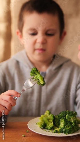 Picky child rejecting healthy green broccoli. Young boy holding a fork of vegetables away from his face with a disgusted expression, showing the authentic struggle of fussy eating in childhood