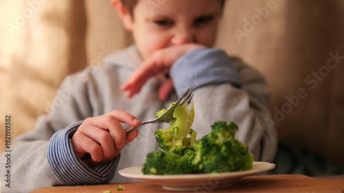 Child refusing to eat broccoli. A young boy expresses dislike and refuses a forkful of green vegetables, illustrating picky eating habits, childhood nutrition struggles, authentic family mealtime
