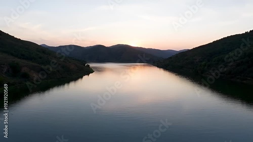 Scenic landscape of calm lake water surrounded by lush green hills at sunset