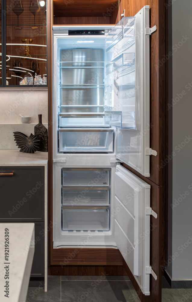 Fototapeta premium Open empty built-in refrigerator with freezer in walnut kitchen cabinet