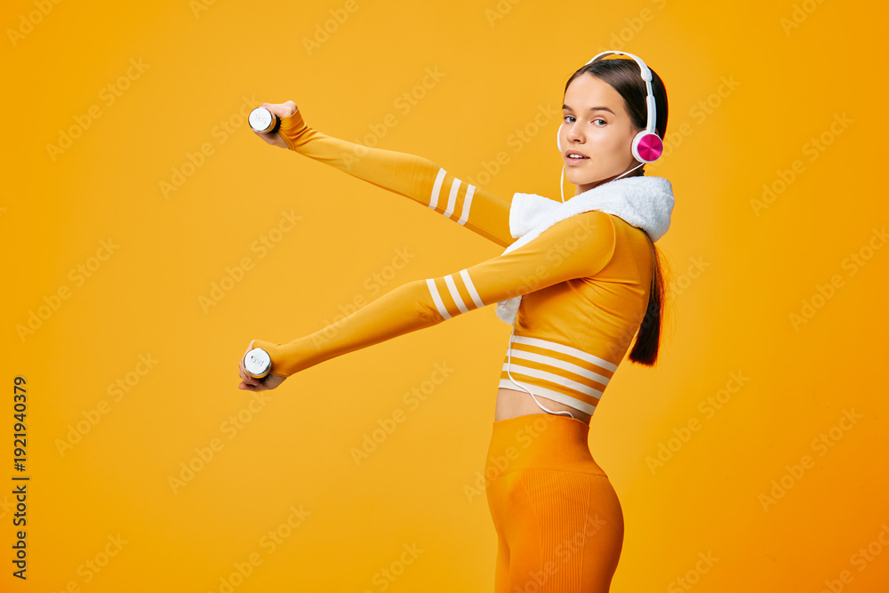 Naklejka premium Woman in bright orange sportwear lifts dumbbells with headphones against a vivid orange backdrop, showcasing fitness, exercise, movement and energetic sport-inspired training.