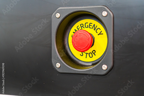 Canvas Print A red emergency stop button, label visible, set against a dark, indistinct backg