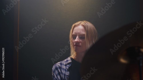Beautiful drummer blonde girl performs solo on stage, sound checking before a rock concert. Woman bangs on a drum kit. Face of female musician bangs drumsticks in a snare drums, cymbals. Portrait