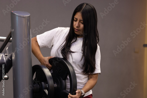 Young woman adding weights to a machine in a modern gym, engaging in a focused workout session to build strength and improve overall physical fitness and health