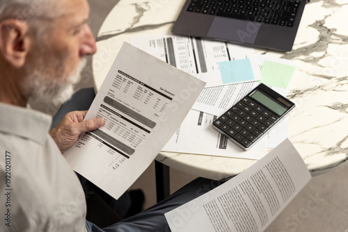 Slika na platnu Man analyzes financial documents and calculates expenses at a table with a lapto