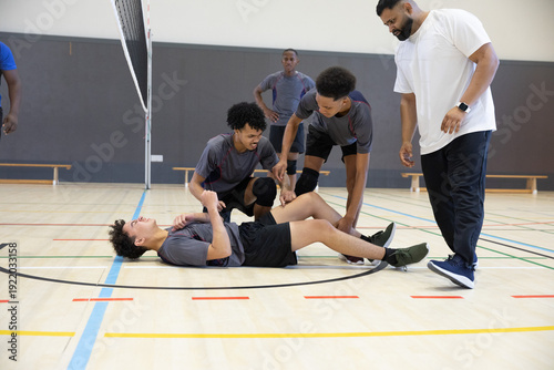 Εκτύπωση καμβά Teenage male players with coach kneeling around injured teammate lying on volley