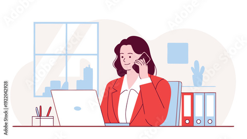 A businesswoman in a red jacket talks on her phone and works on a laptop at her desk in a bright office.