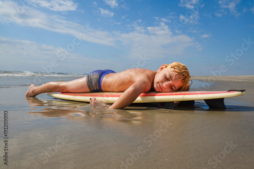 Quadro su tela Boy at beach lying on surfboard with eyes closed