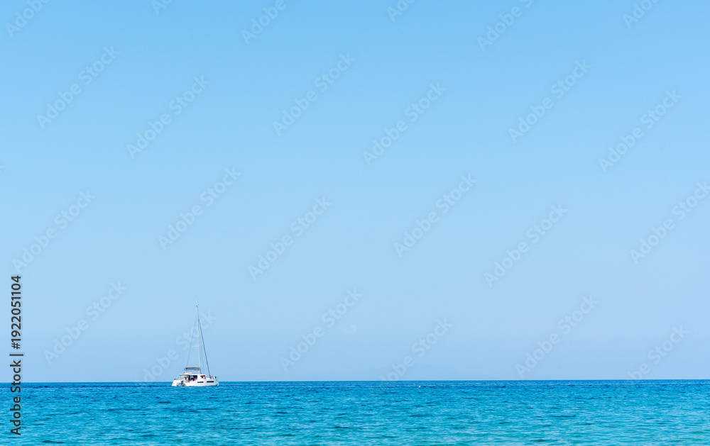 Fototapeta premium Lone white sailboat anchored on vast calm turquoise Adriatic sea under clear bright blue sky with minimalist horizon. Concept of freedom, solitude, luxury sailing vacation and Mediterranean serenity.