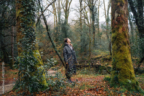 Person in a raincoat looking up in a dense forest